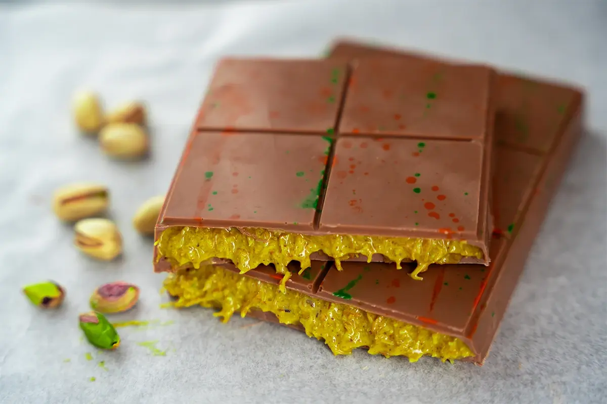 A rich milk chocolate bar filled with a vibrant yellow pistachio-flavored filling, decorated with colorful splashes.